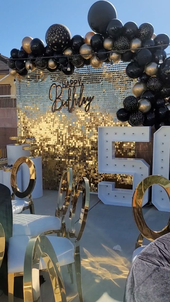Gold sequin backdrop with black and gold balloons and large illuminated 50 numbers.