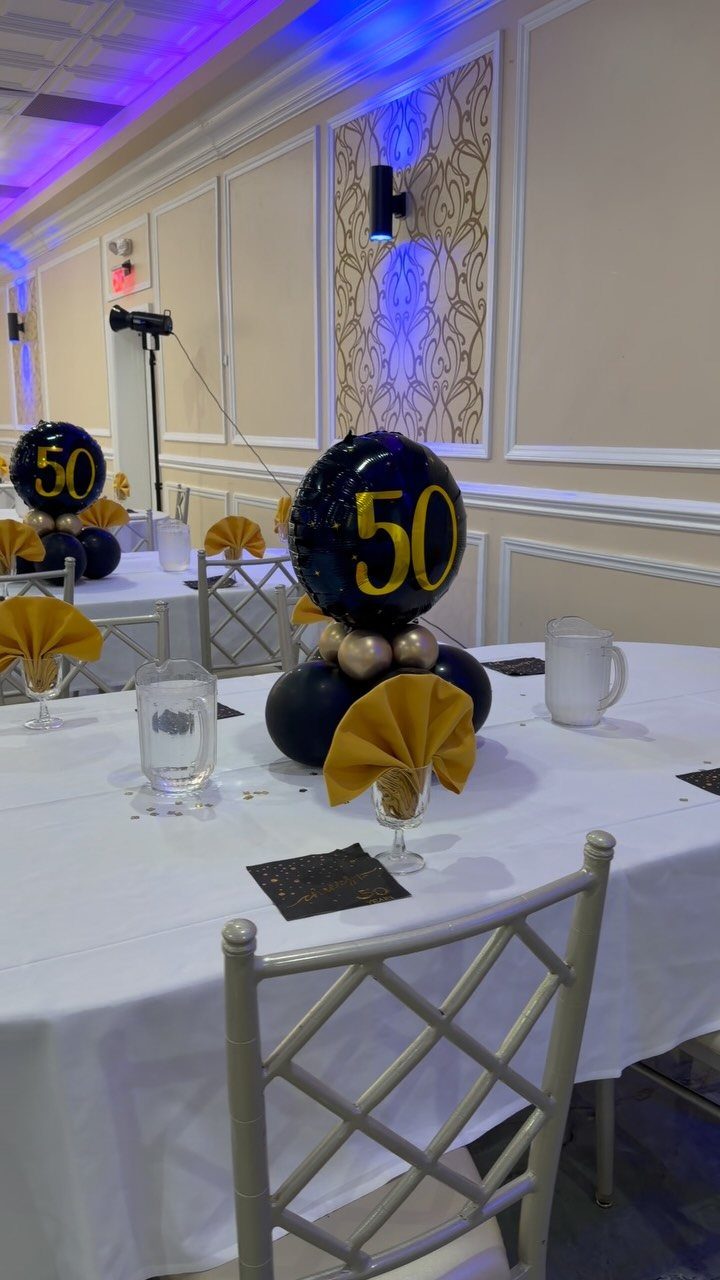 Banquet table with black and gold 50th birthday balloon centerpieces and gold napkins.