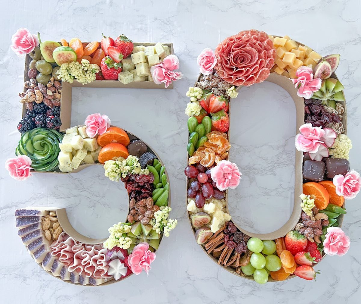 Charcuterie board shaped like the number 50 with fruits, cheeses, and flowers.