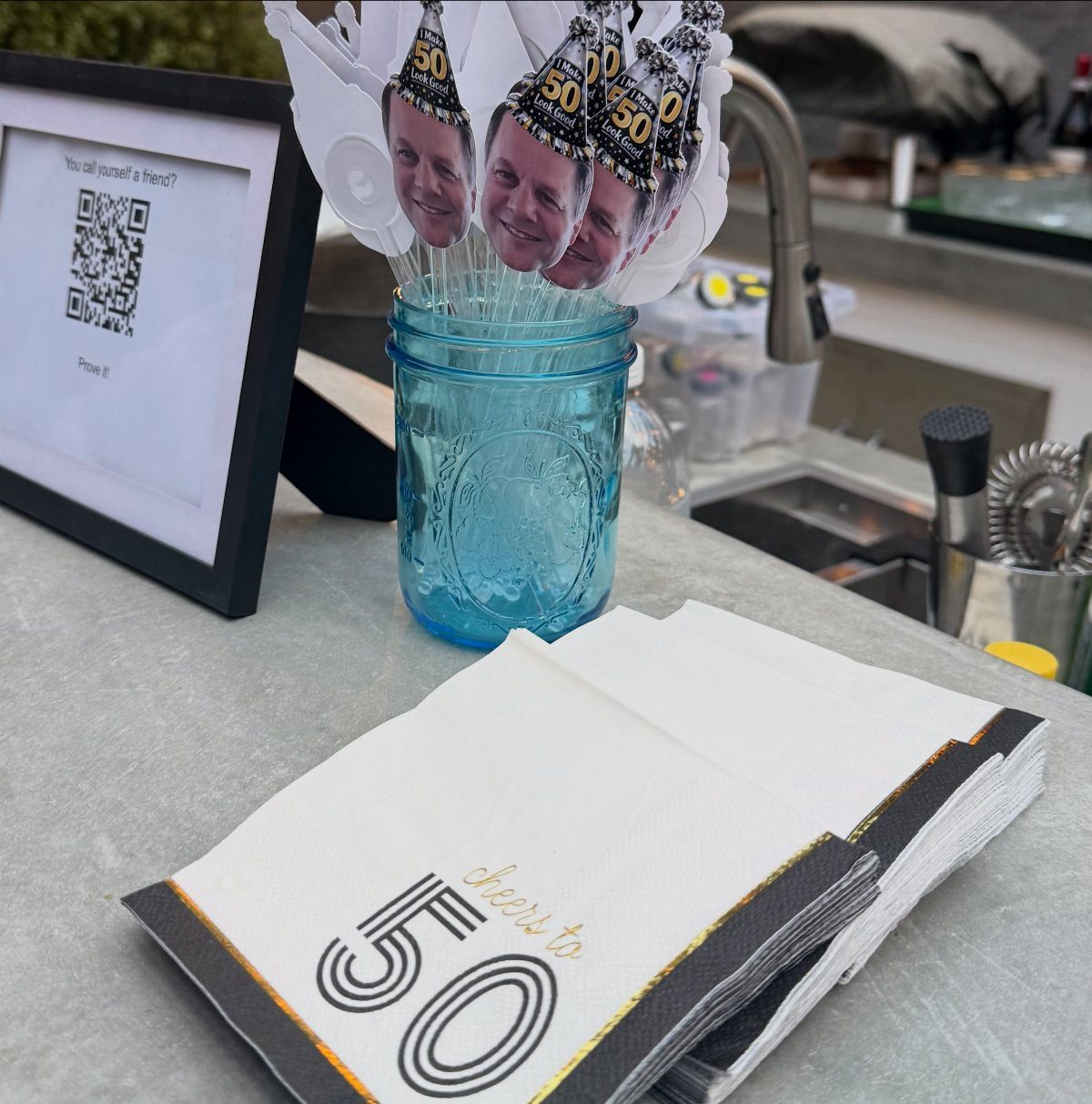 Party napkins with cheers to 50 text and photo cutouts in blue jar
