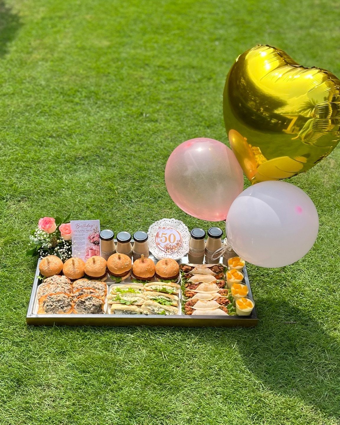 Food platter and balloons on green grass for a 50th birthday picnic party