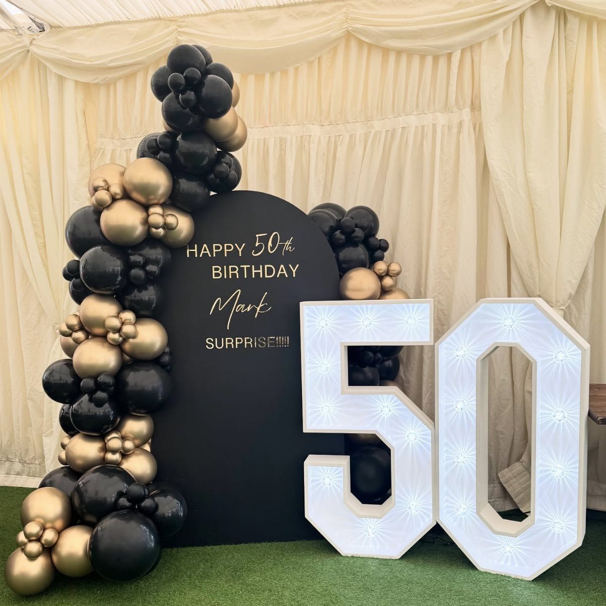 Black and gold balloon arch with illuminated number 50 for a birthday party.