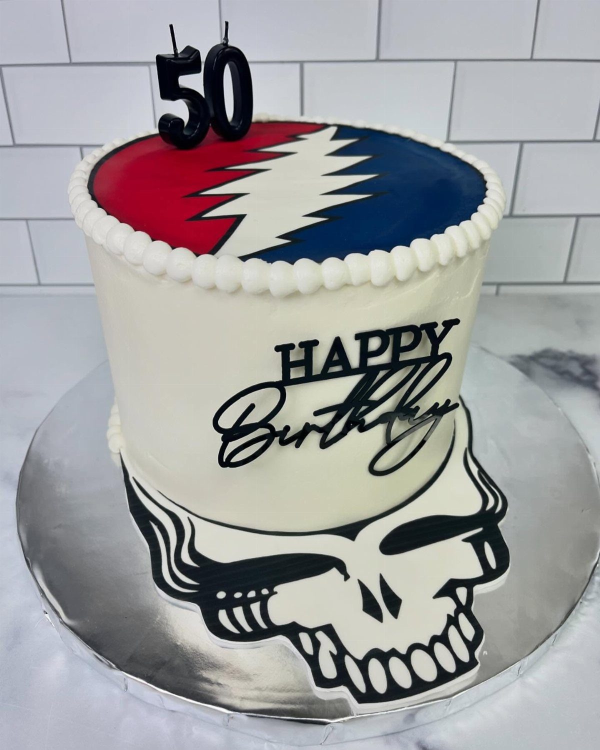 White birthday cake with 50 candles and Grateful Dead themed decorations.