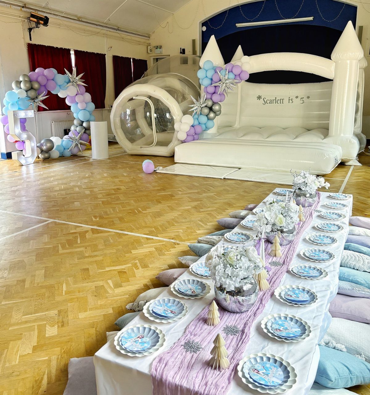 White inflatable bouncy castle and party table with blue and purple decorations.