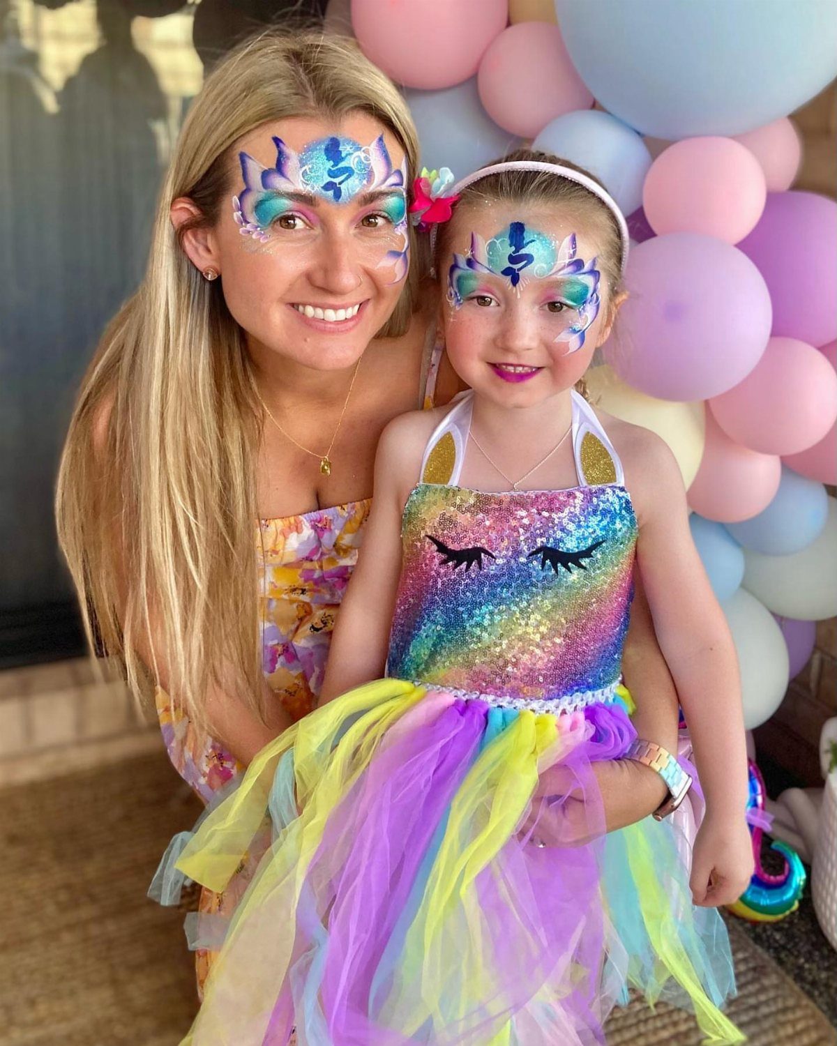 Woman and young girl with colorful face paint and rainbow tutu party attire.