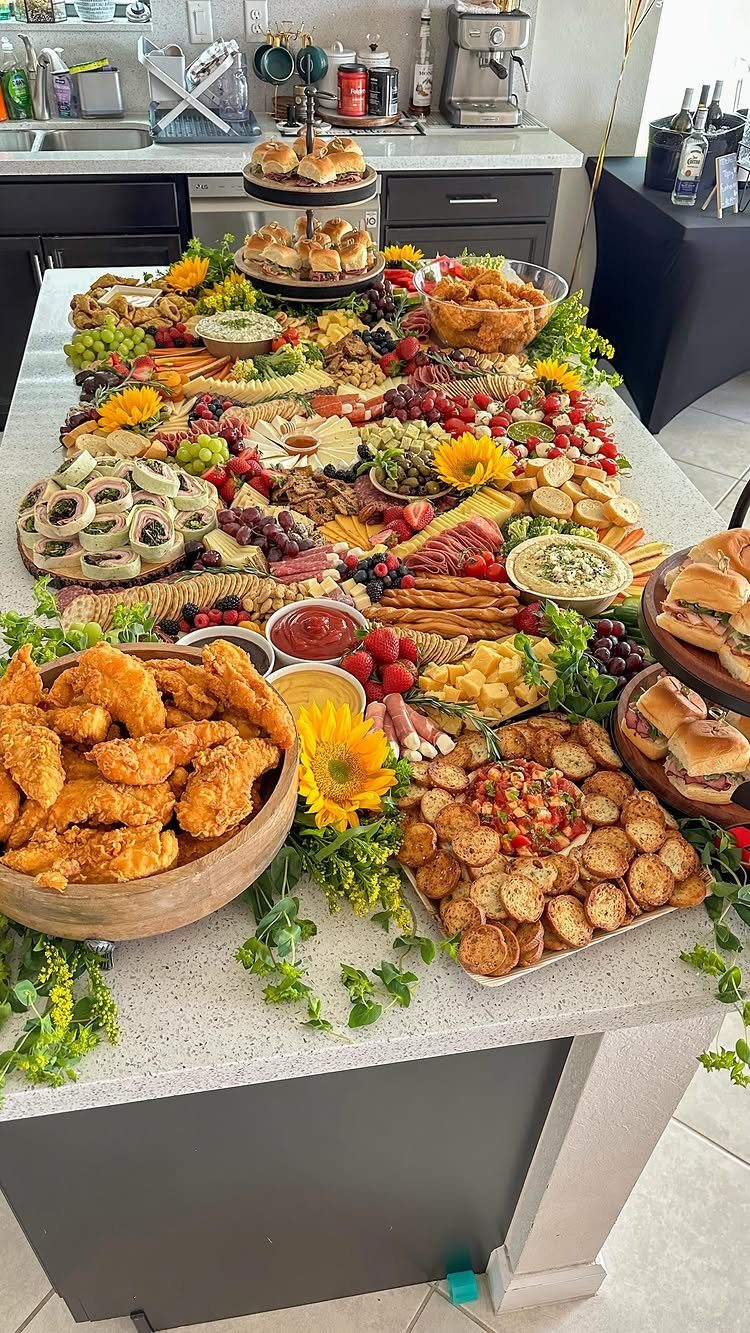 Elaborate food graze board with fried chicken, sliders, and fruit on a kitchen island.