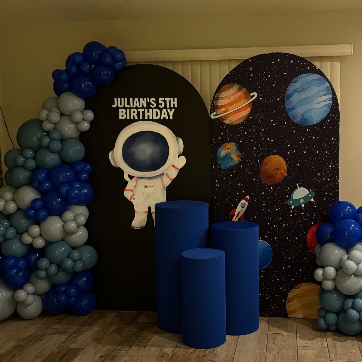 Space-themed birthday party decorations with blue balloons and astronaut backdrop for fifth birthday.