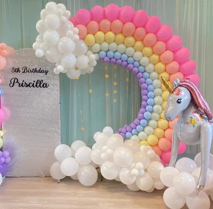 Balloon rainbow arch with white clouds and a unicorn for a 5th birthday.