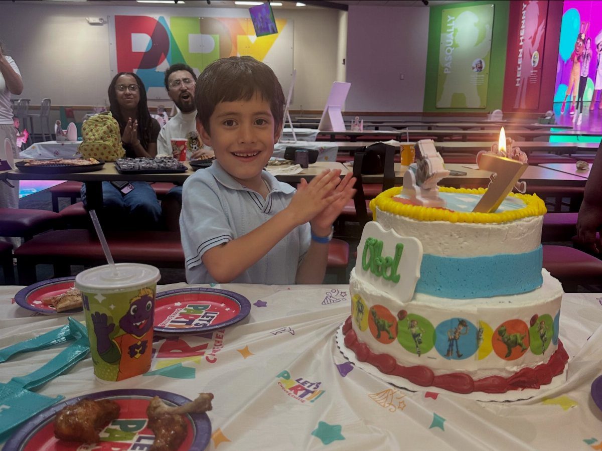 Smiling boy celebrating his seventh birthday with a cake at an arcade venue.