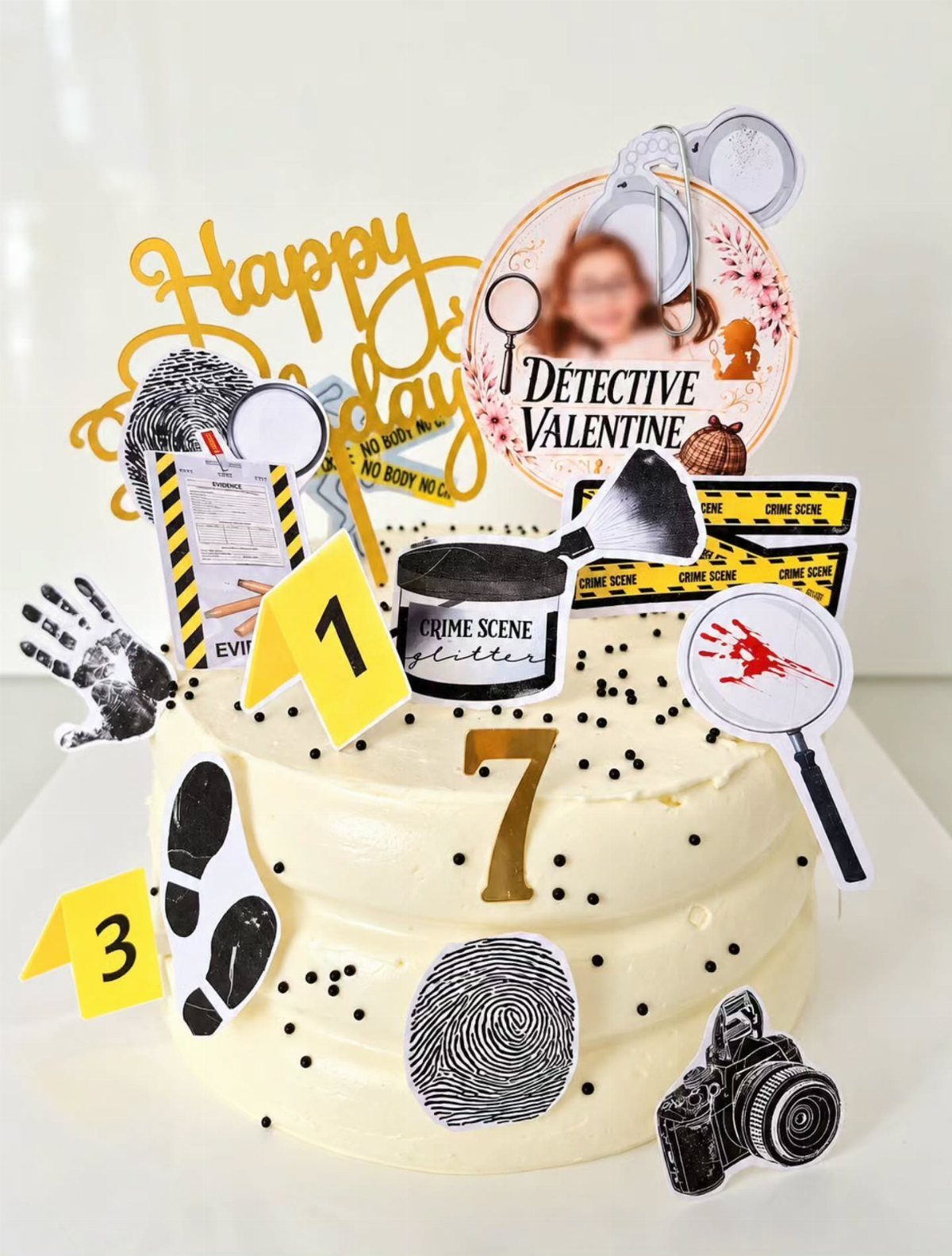 Detective themed birthday cake with crime scene tape, fingerprints, and magnifying glass toppers.