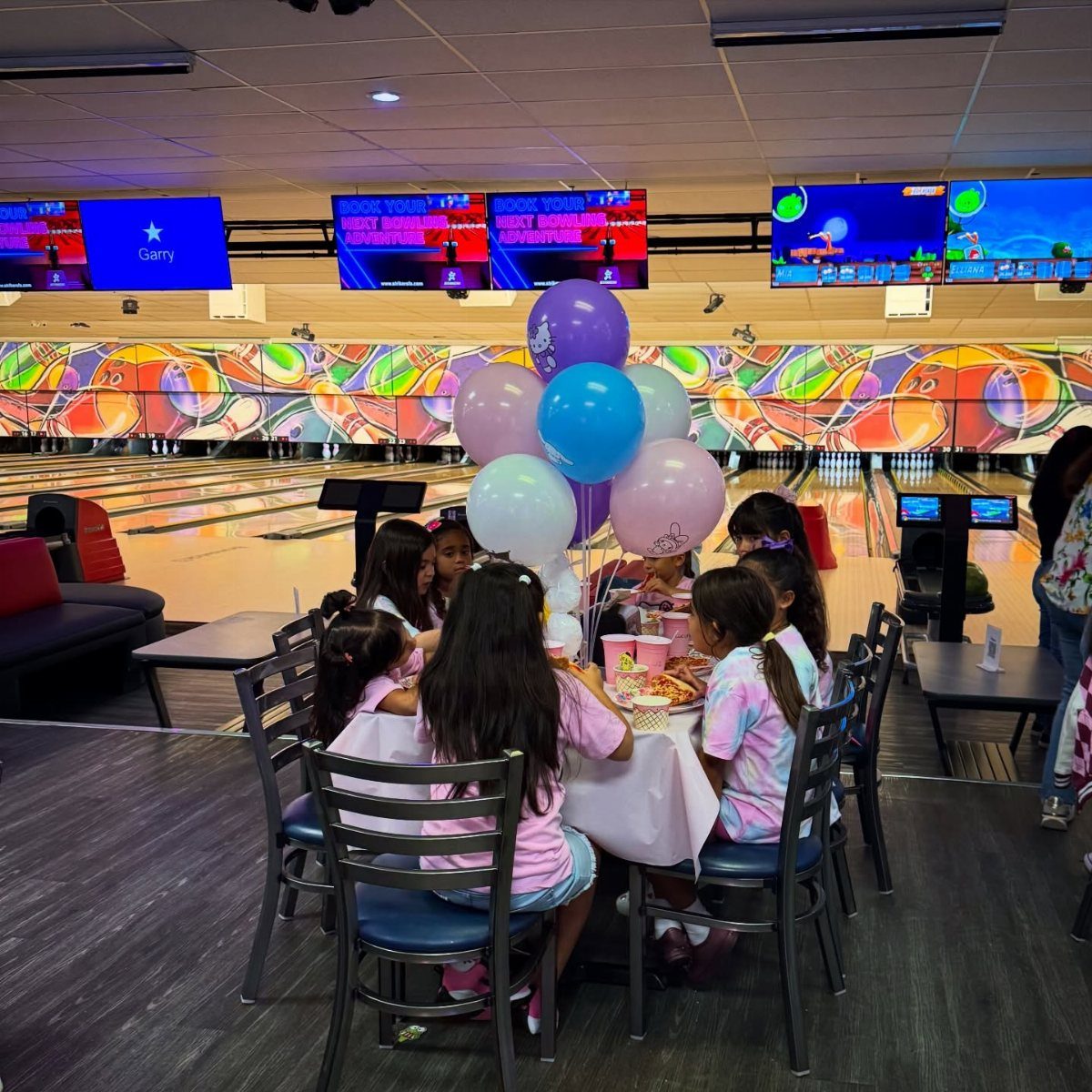 Young girls celebrating at a table with balloons inside a bowling alley.