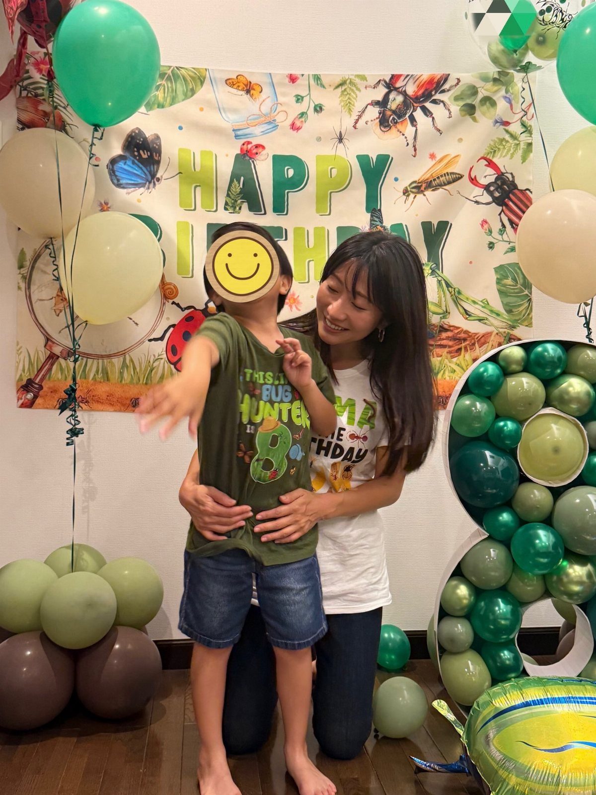 Woman and boy posing before a bug-themed birthday banner with green balloons.