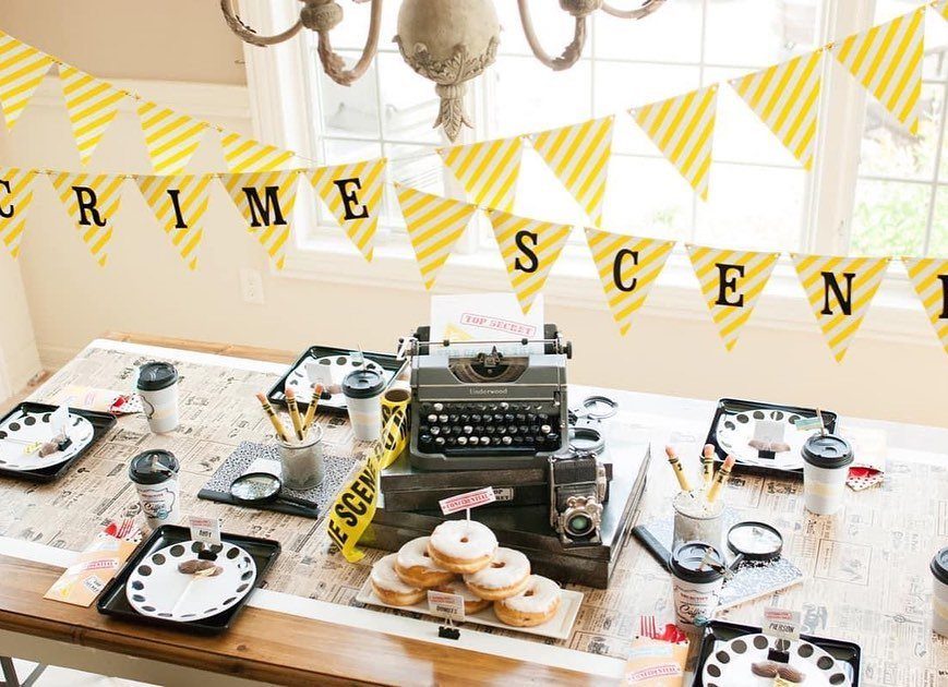 Crime scene themed party table with vintage typewriter, camera, and yellow caution banner.