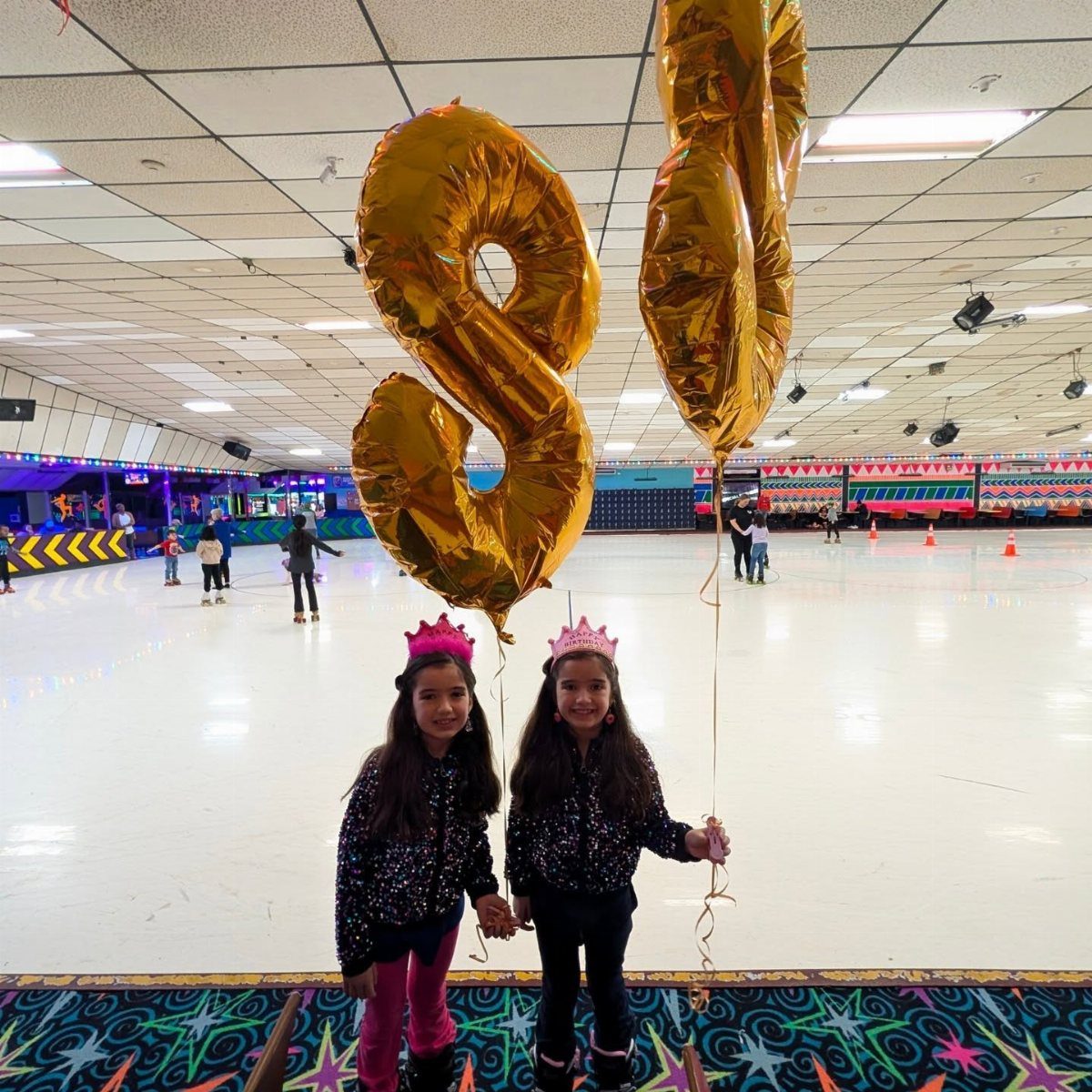 Two girls with gold number 8 balloons standing in a roller skating rink.