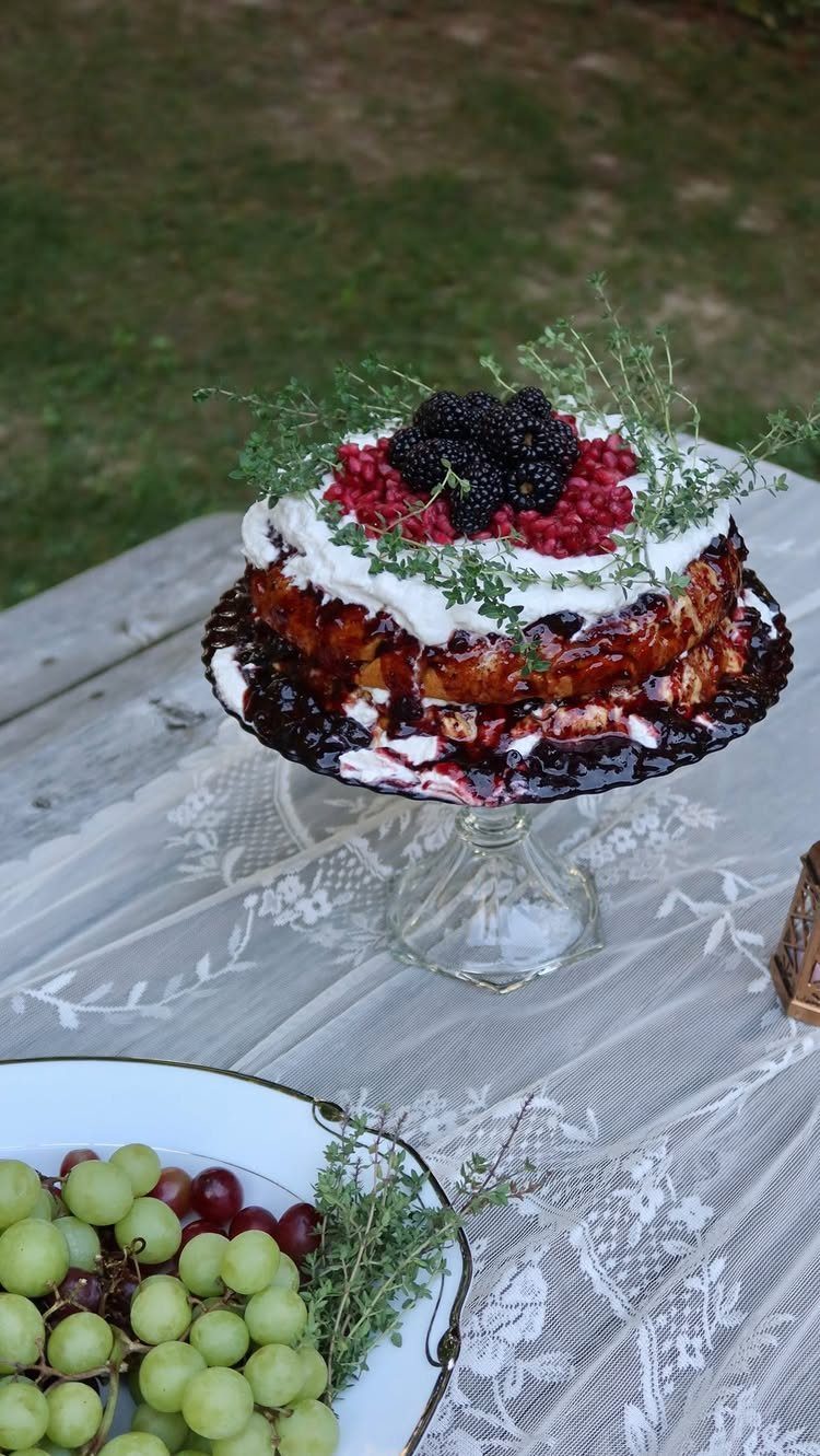 Layered berry cake on a glass stand with grapes on a lace tablecloth.