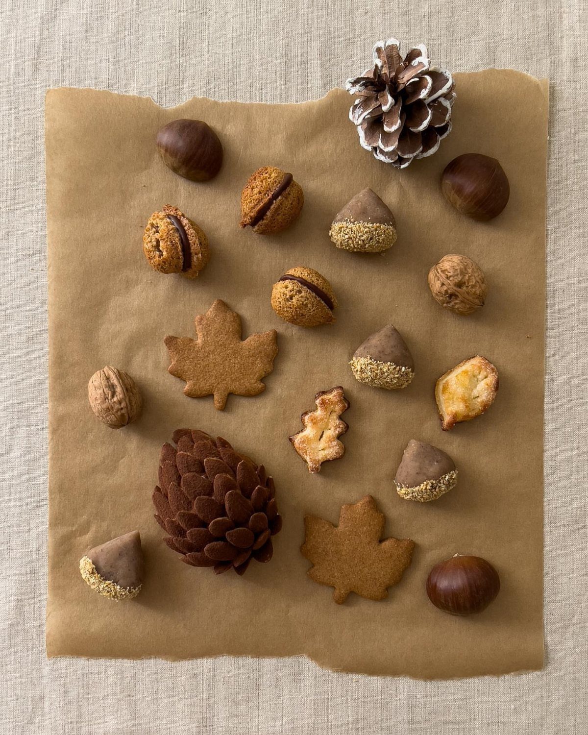 Autumn-themed cookies and nuts with pinecones arranged on brown parchment paper.