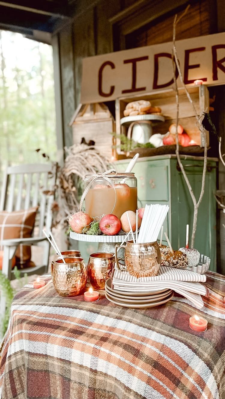 Apple cider station with copper mugs and red apples on a plaid tablecloth.