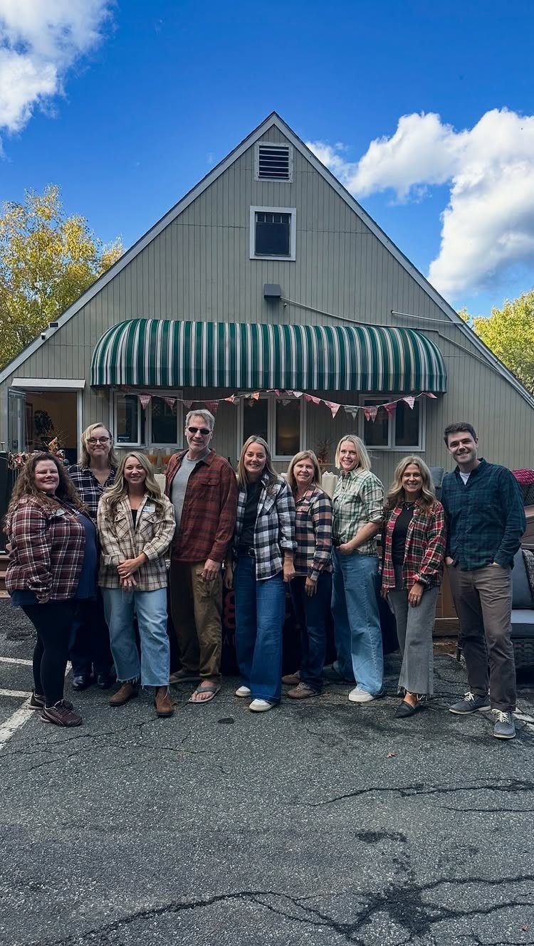 Group of adults wearing plaid flannel shirts posing in front of a grey house.