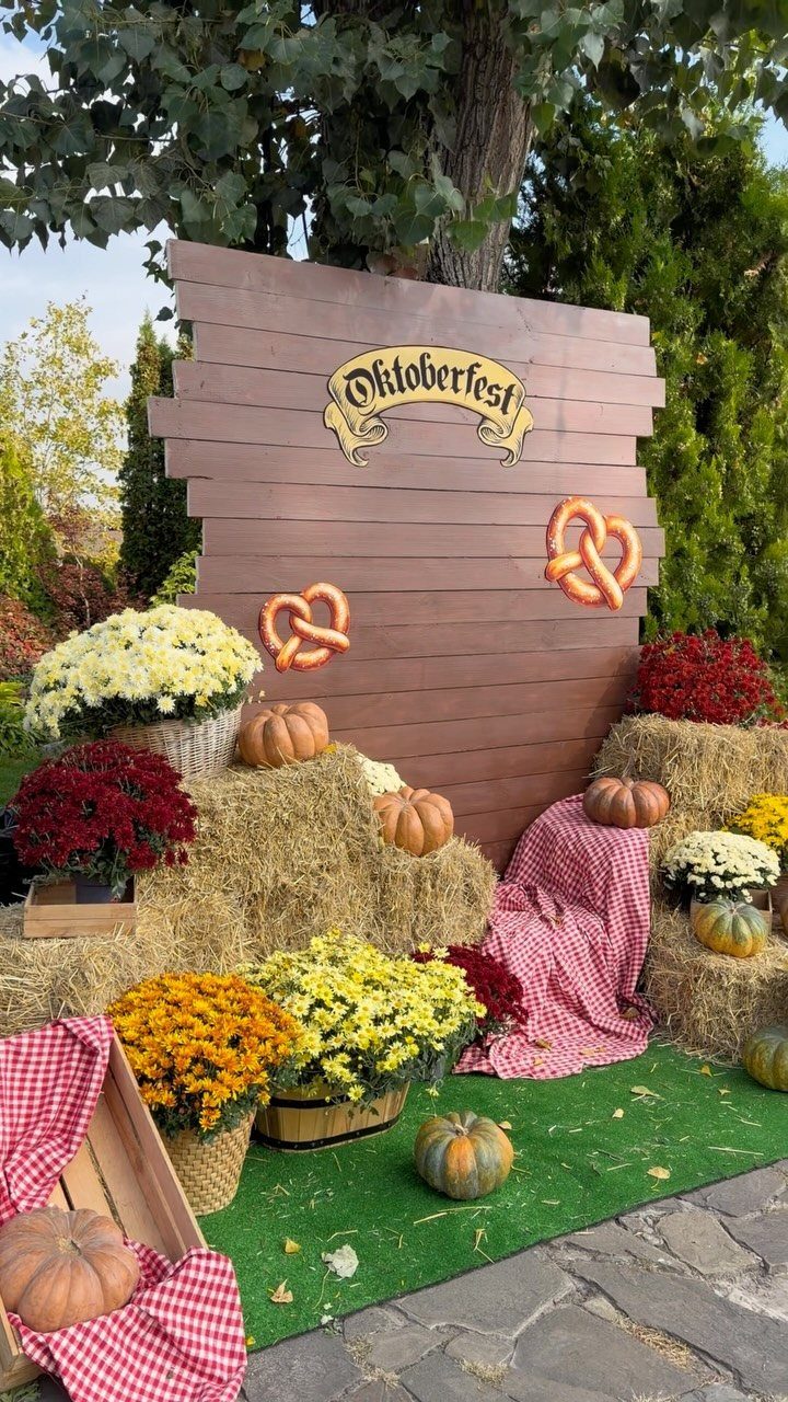 Oktoberfest backdrop with wooden panels, pumpkins, hay bales, and colorful autumn flowers.