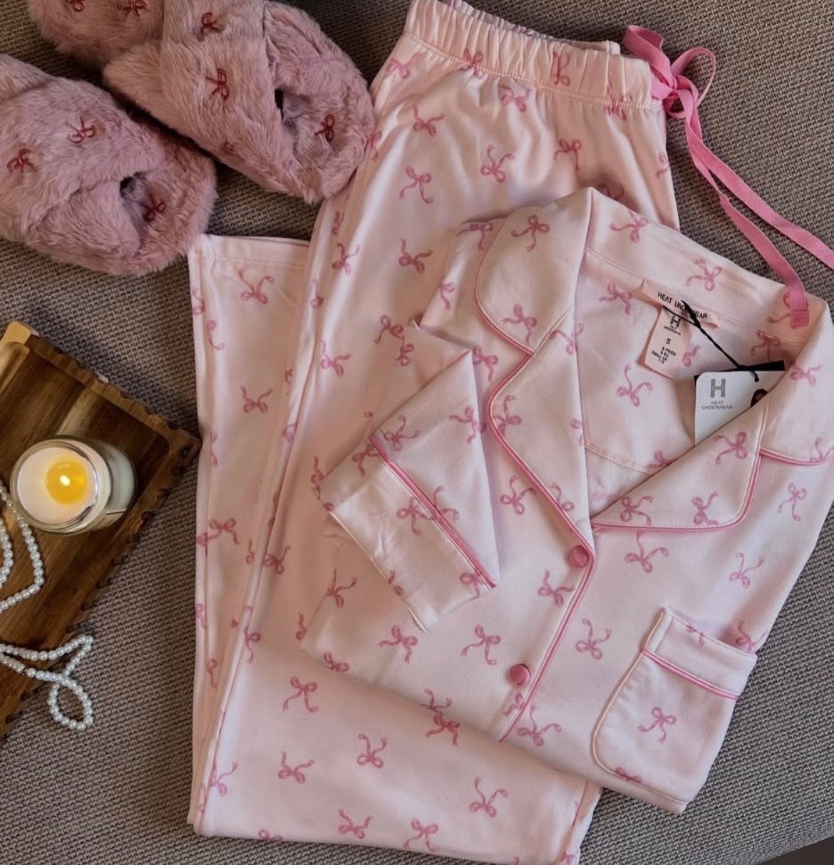 Pink pajama set with bow patterns, fluffy slippers, and a lit candle.
