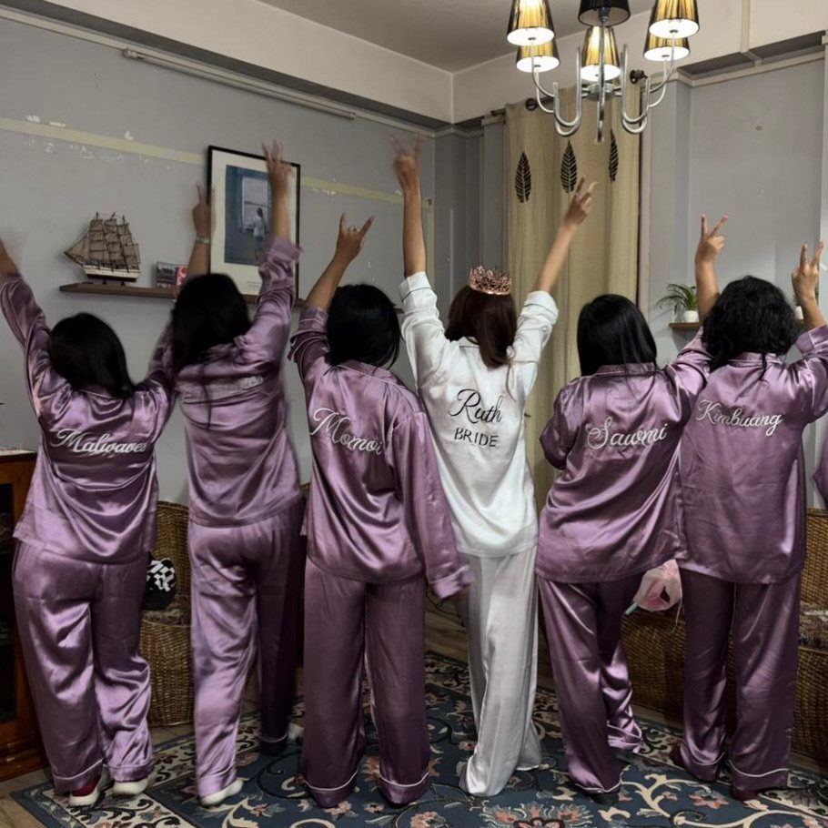 Six women in satin long sleeve pajamas posing with their backs to the camera.