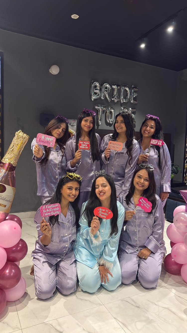 Seven women in satin pajamas posing with pink balloons and bride-to-be balloons.