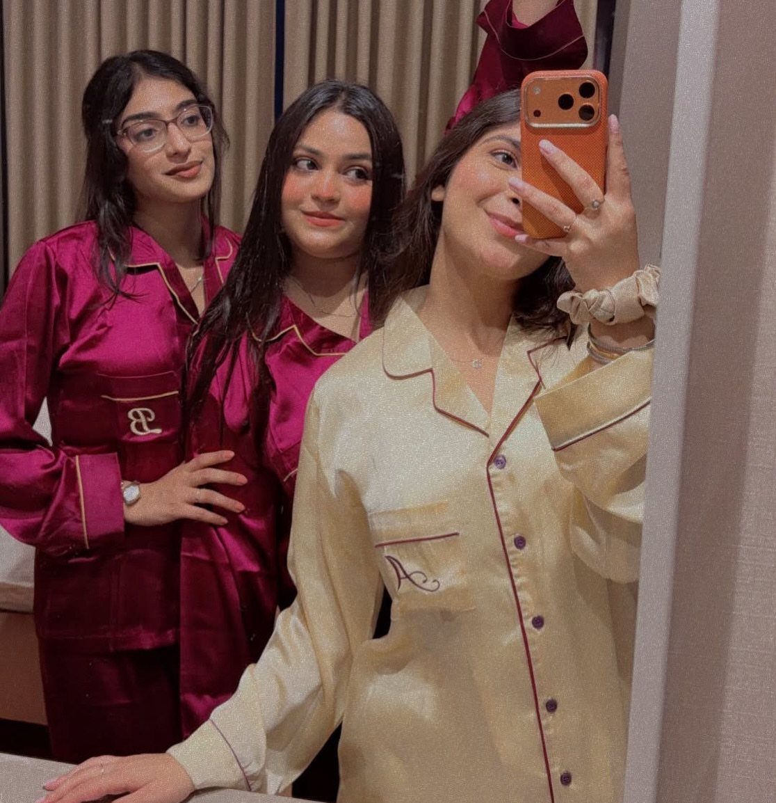 Three women wearing satin pajama sets in magenta and champagne colors posing for selfie.