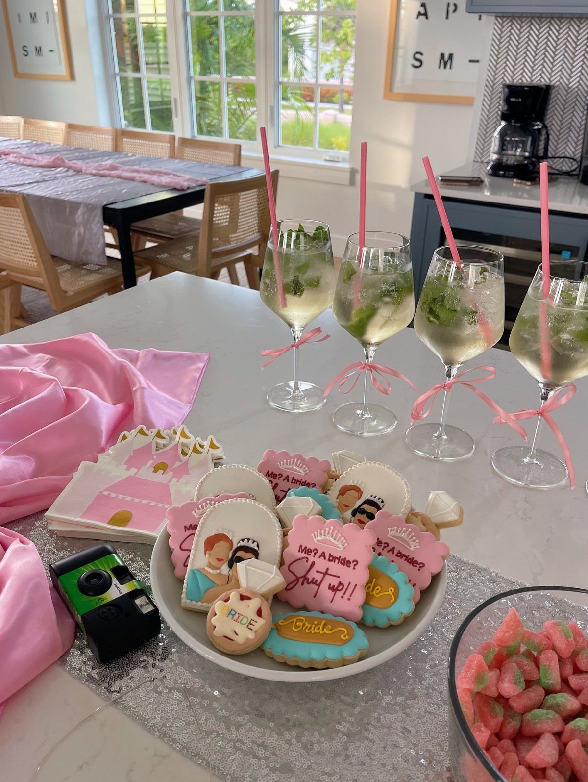 Bridal themed sugar cookies and mojitos with pink ribbons on a white counter.