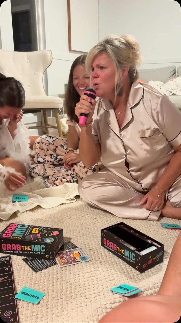 Women in pajamas playing a microphone game while sitting on a white rug.