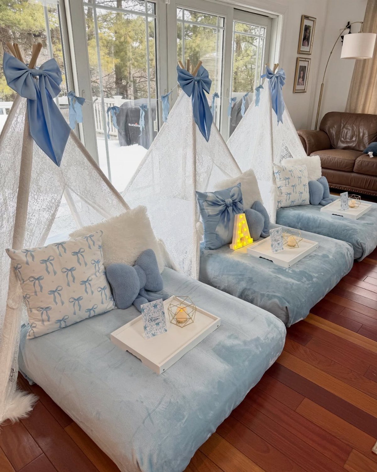 Three white lace teepees with blue accents and plush bedding on wooden floors.