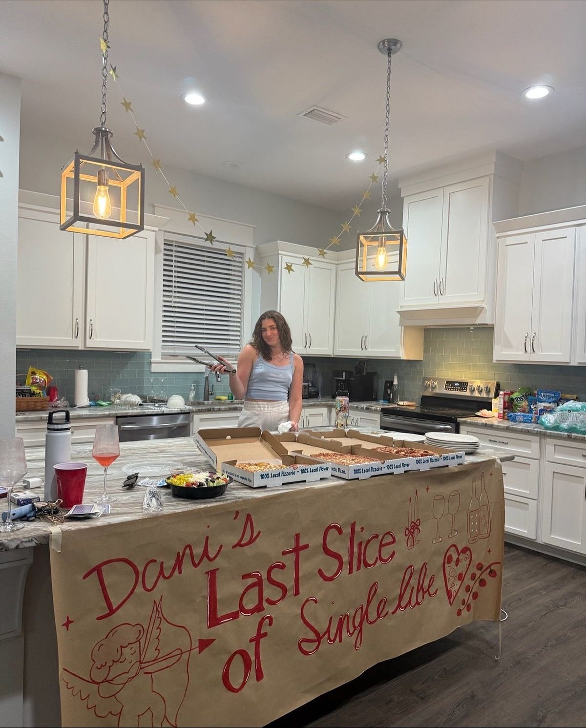 Woman standing behind a bachelorette party pizza spread with a custom paper banner.