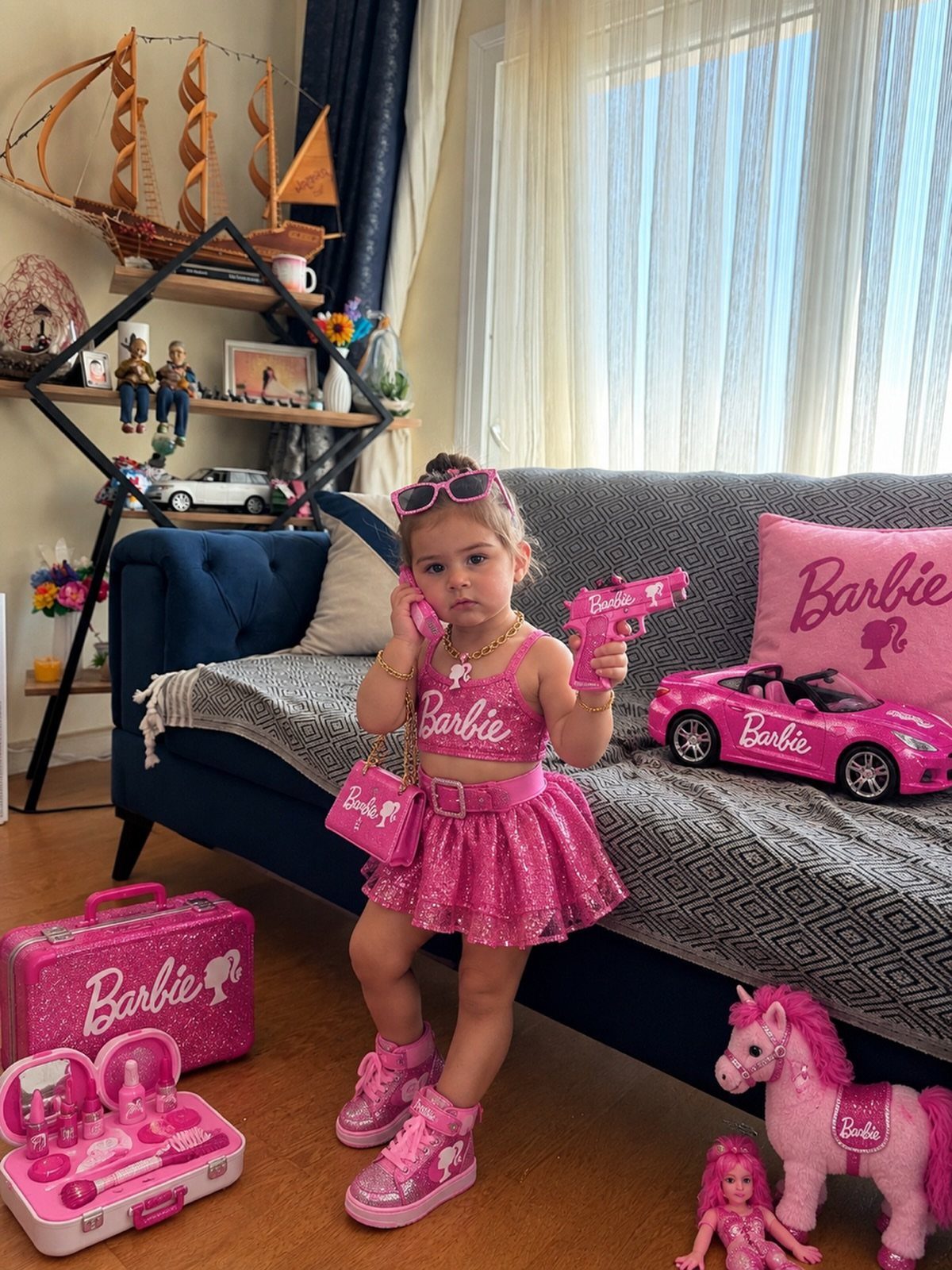 Young girl in sparkly pink Barbie outfit posing with pink toys in a living room