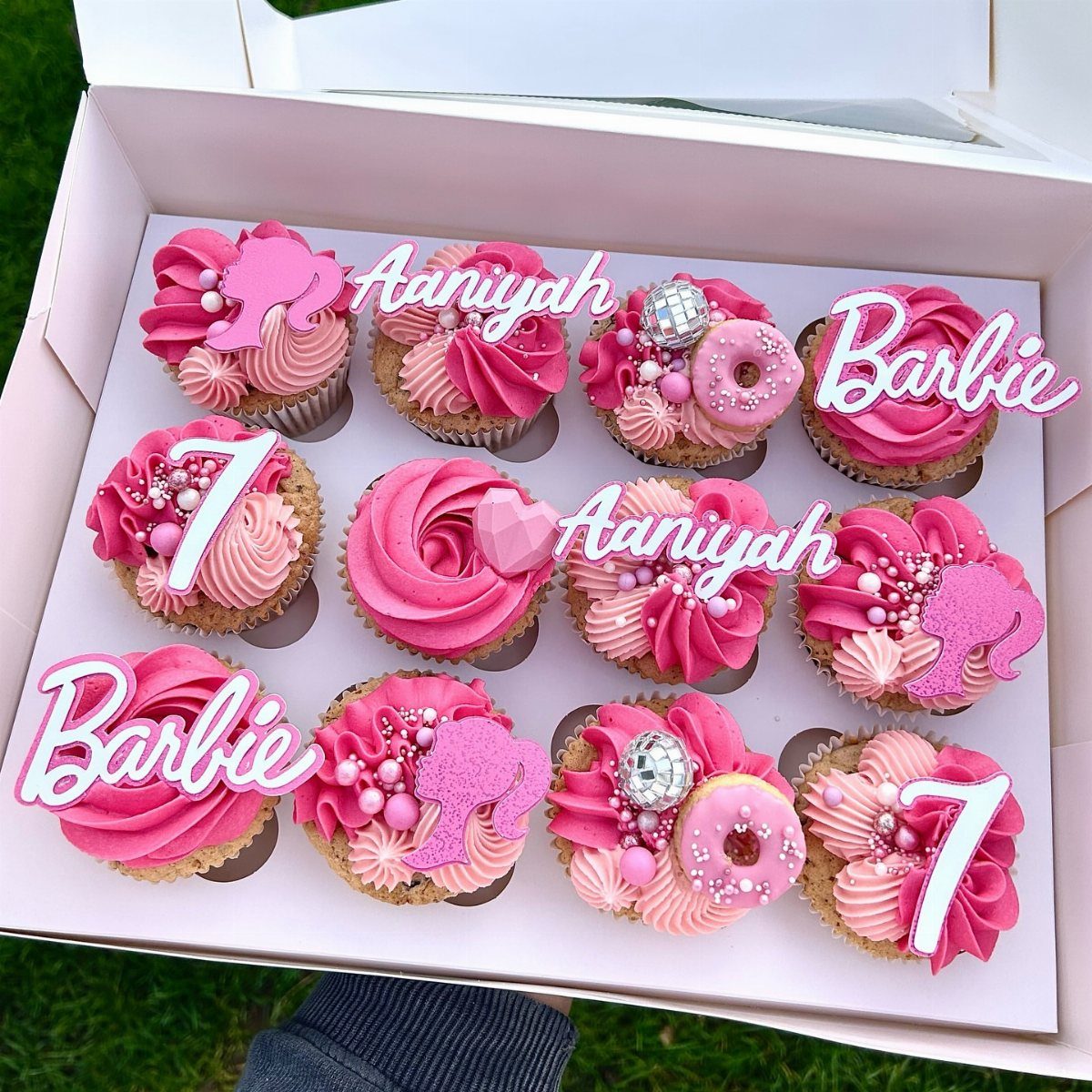 Pink frosted cupcakes with Barbie silhouettes, the name Aaniyah, and number 7 toppers.