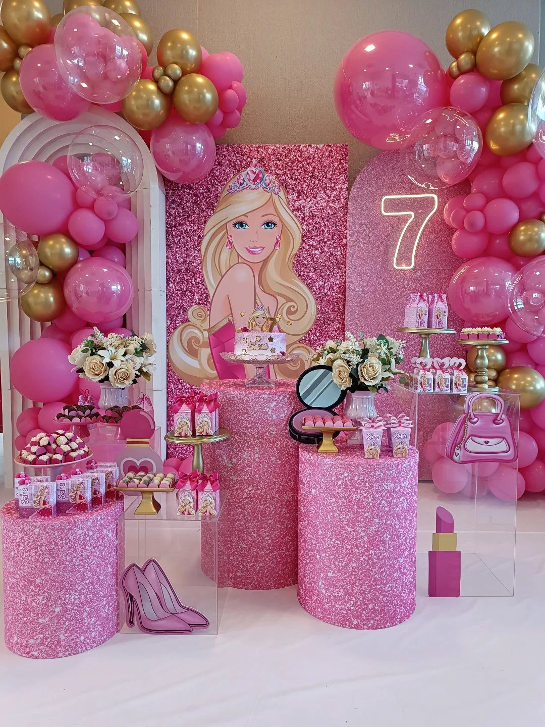 Barbie themed party decorations with pink glitter pedestals, balloons, and a Barbie backdrop.