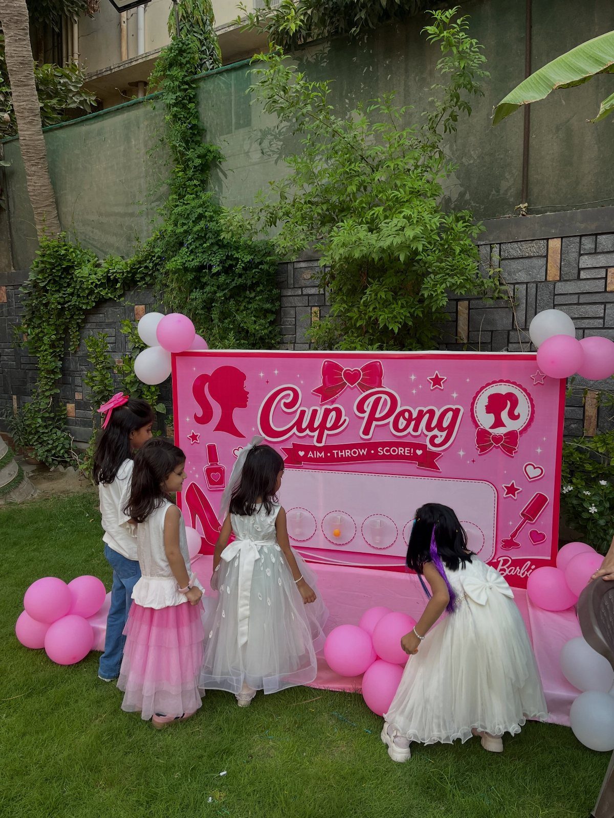Young girls playing Barbie themed cup pong game at an outdoor birthday party