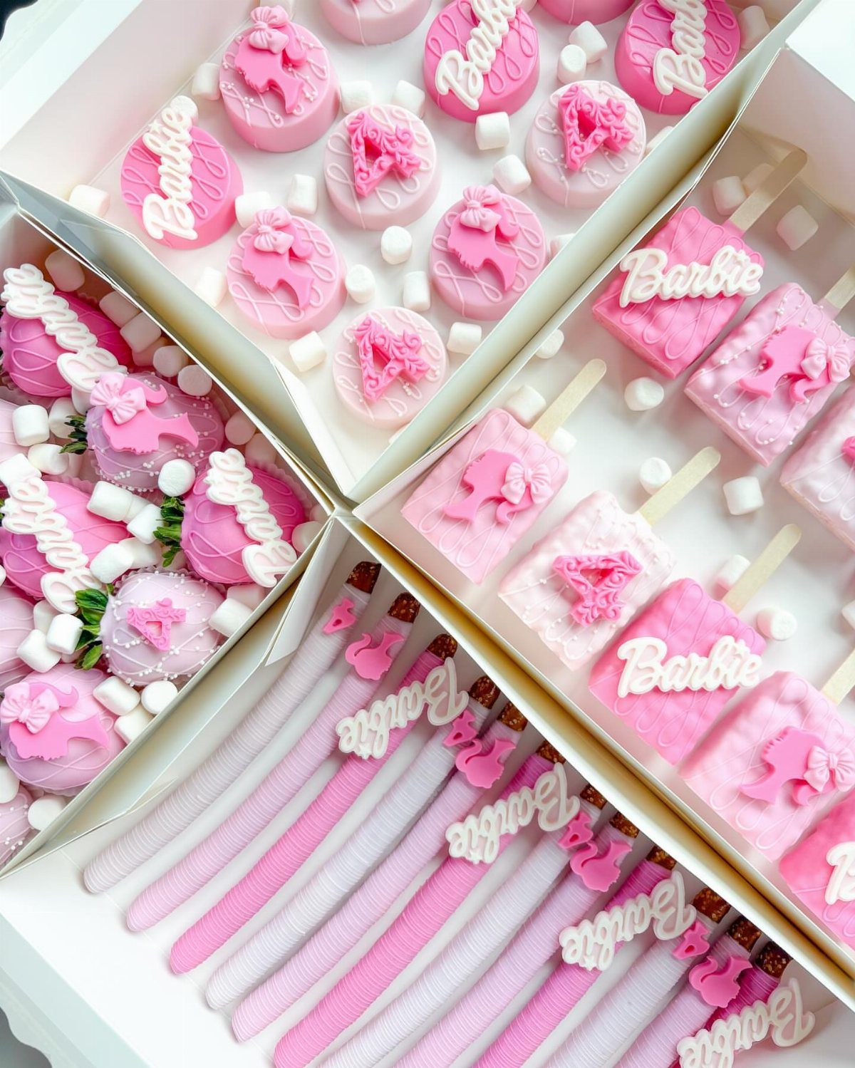 Pink Barbie-themed chocolates, cake pops, and wafer sticks arranged in a white tray.