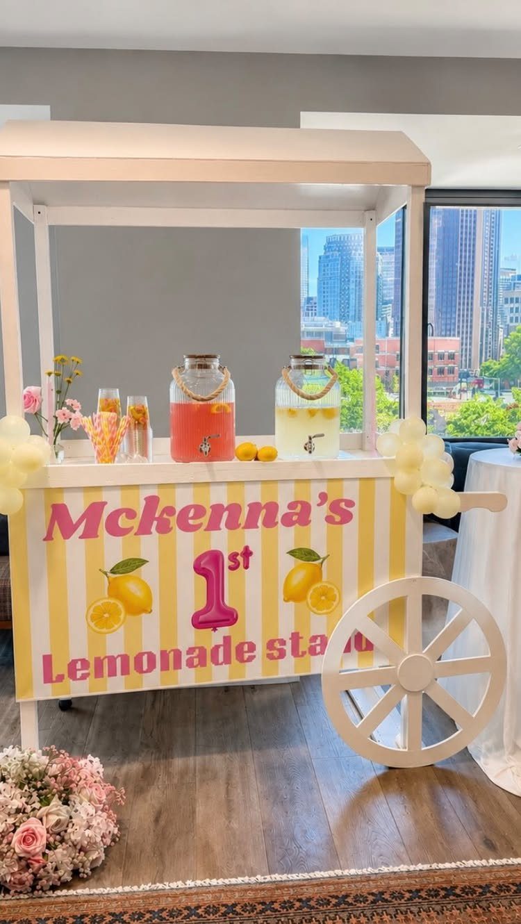 White lemonade stand with pink and yellow drinks and a striped banner.