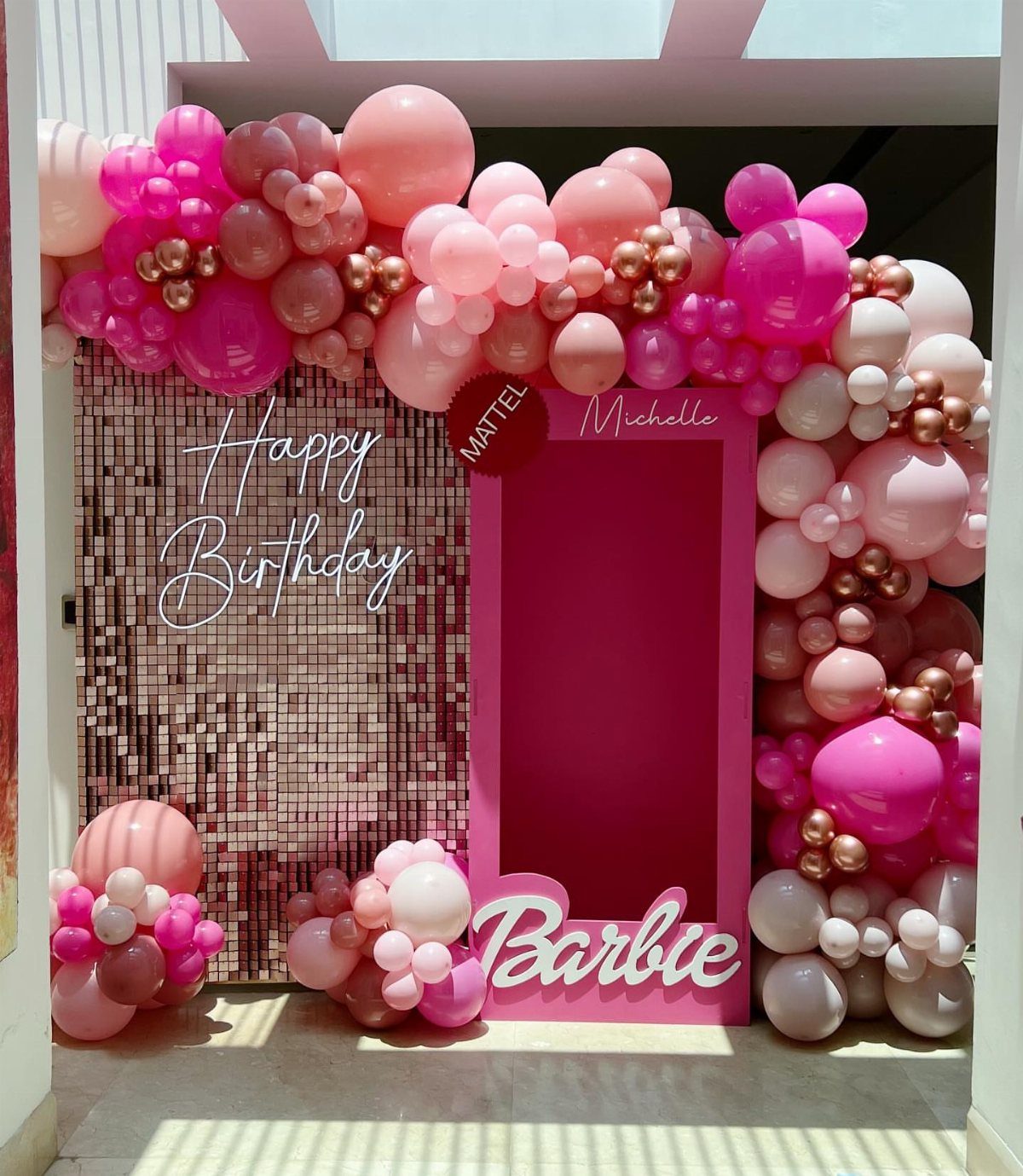 Pink and gold balloon garland framing a Barbie box and sequin backdrop.