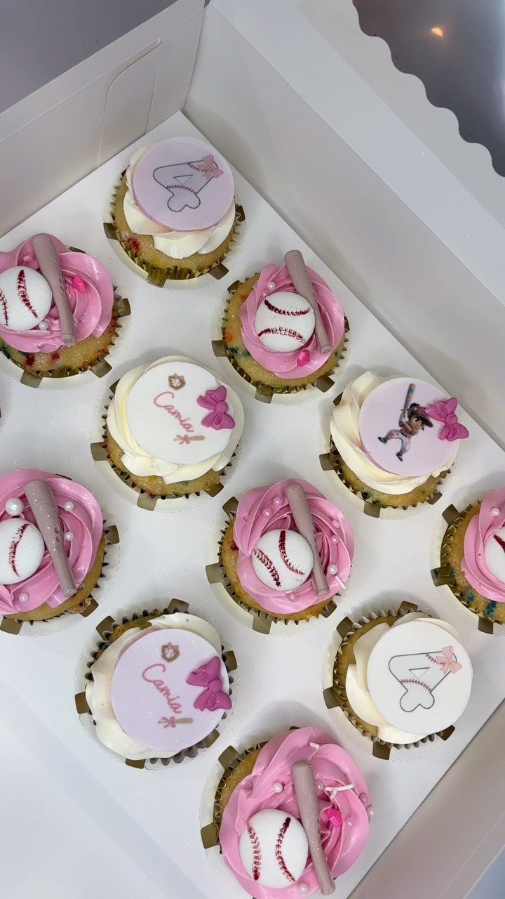 Cupcakes with pink frosting topped with miniature baseballs, bats, and personalized name discs.