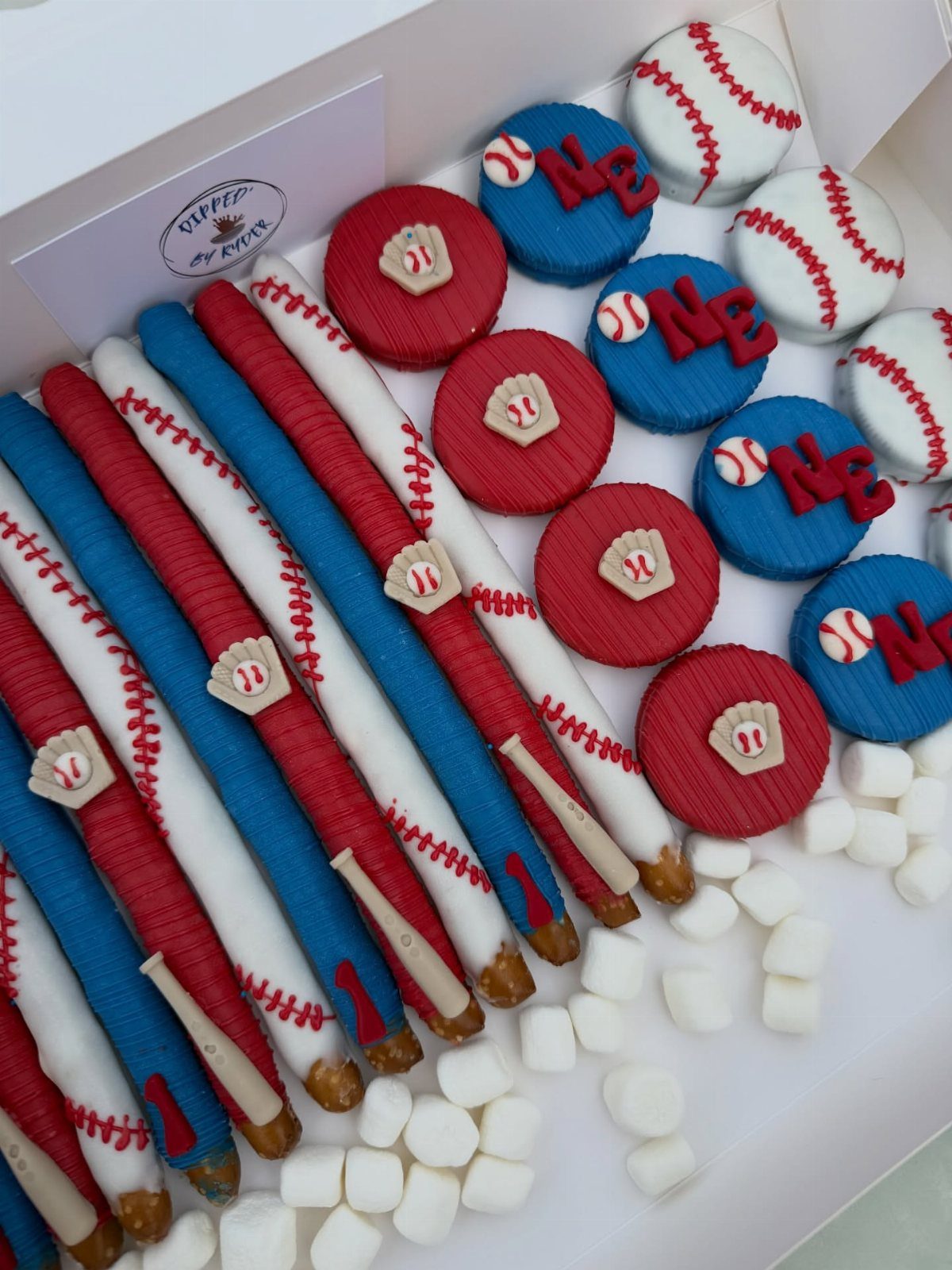 Baseball-themed chocolate treats including pretzel bats and round candies in a white box.