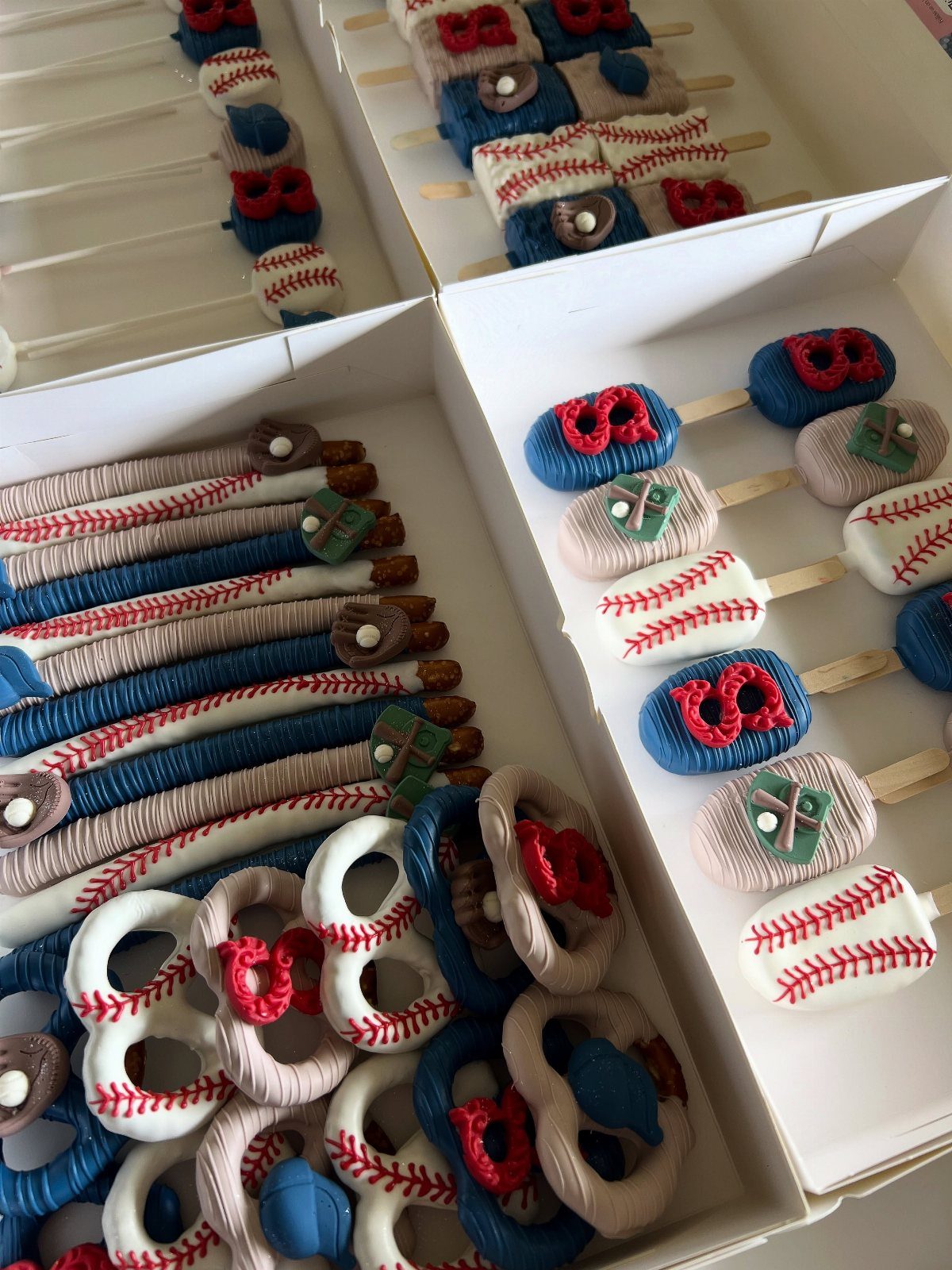 Baseball-themed cake pops and pretzels decorated as baseballs, gloves, and jerseys in boxes.