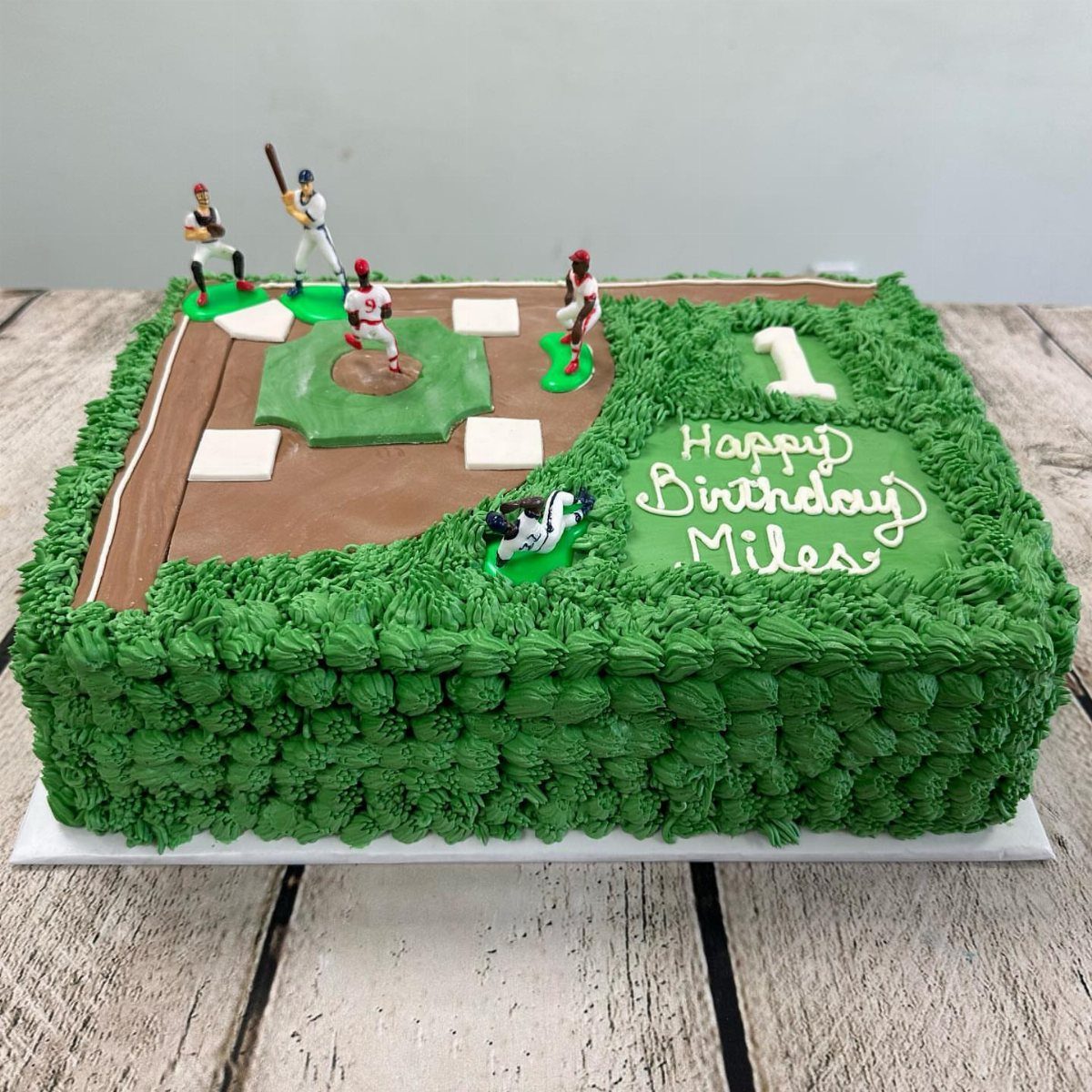 Baseball diamond cake with green frosting, brown dirt, and small player figurines.