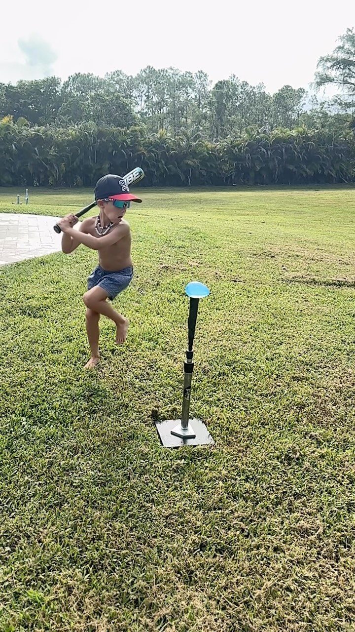 Young boy jumping with a plastic bat next to a batting tee outdoors.