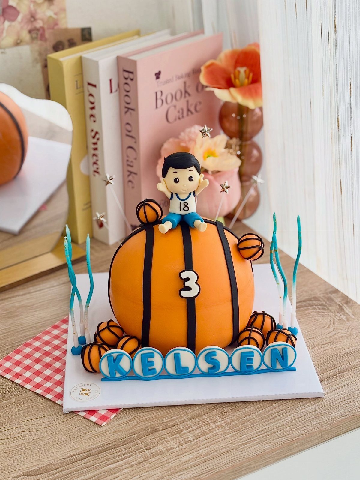 Spherical basketball cake with a small player figure and blue name letters.