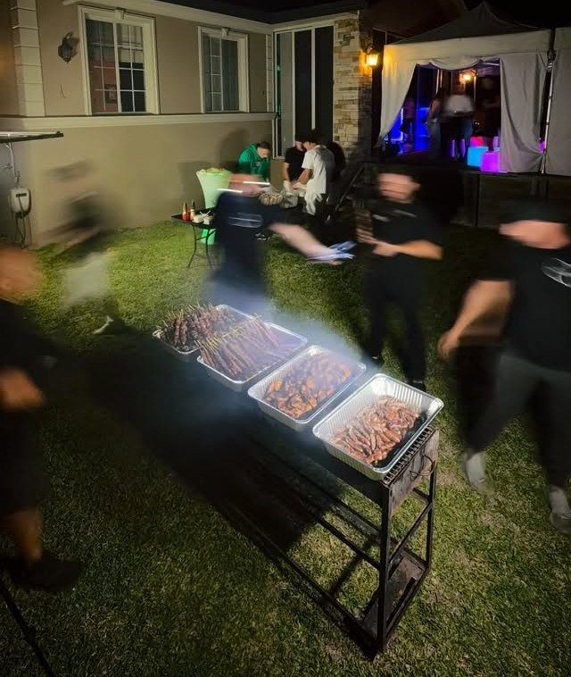 Grilled meat skewers on a long table during a nighttime backyard party.