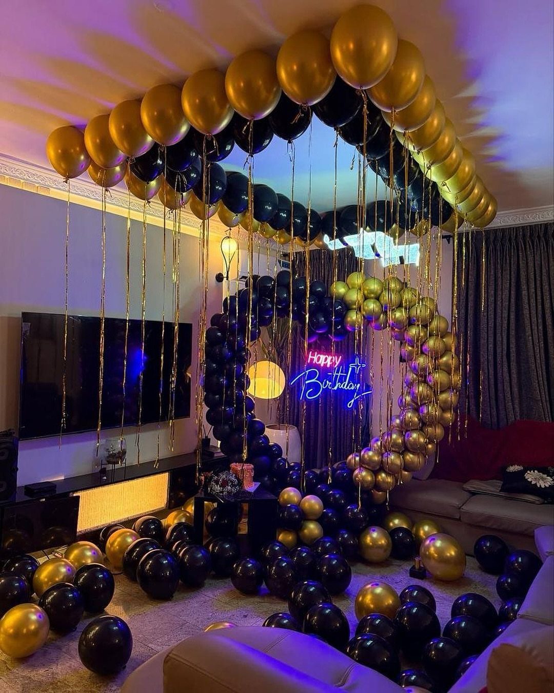 Gold and black balloon decorations with a neon Happy Birthday sign in a living room