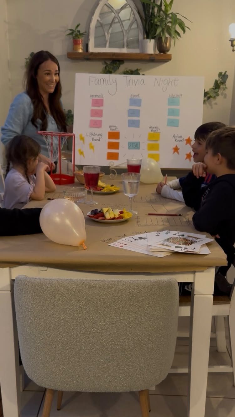 Family playing trivia around a dining table with a scoring board in background