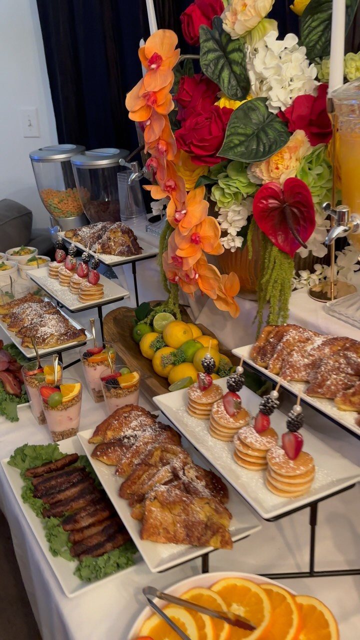 Brunch buffet spread with French toast, mini pancakes, bacon, and colorful floral arrangement.
