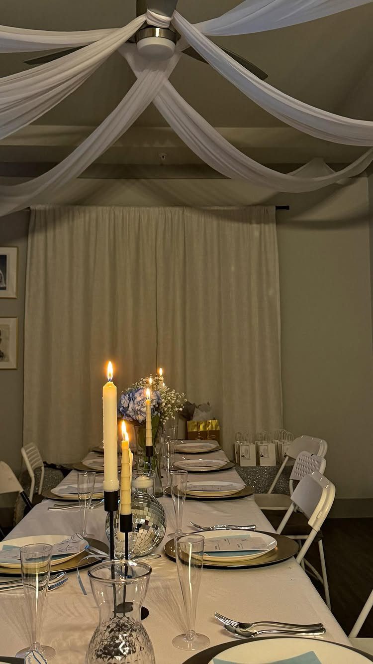Formal dining table set with white linens, gold chargers, and lit taper candles.