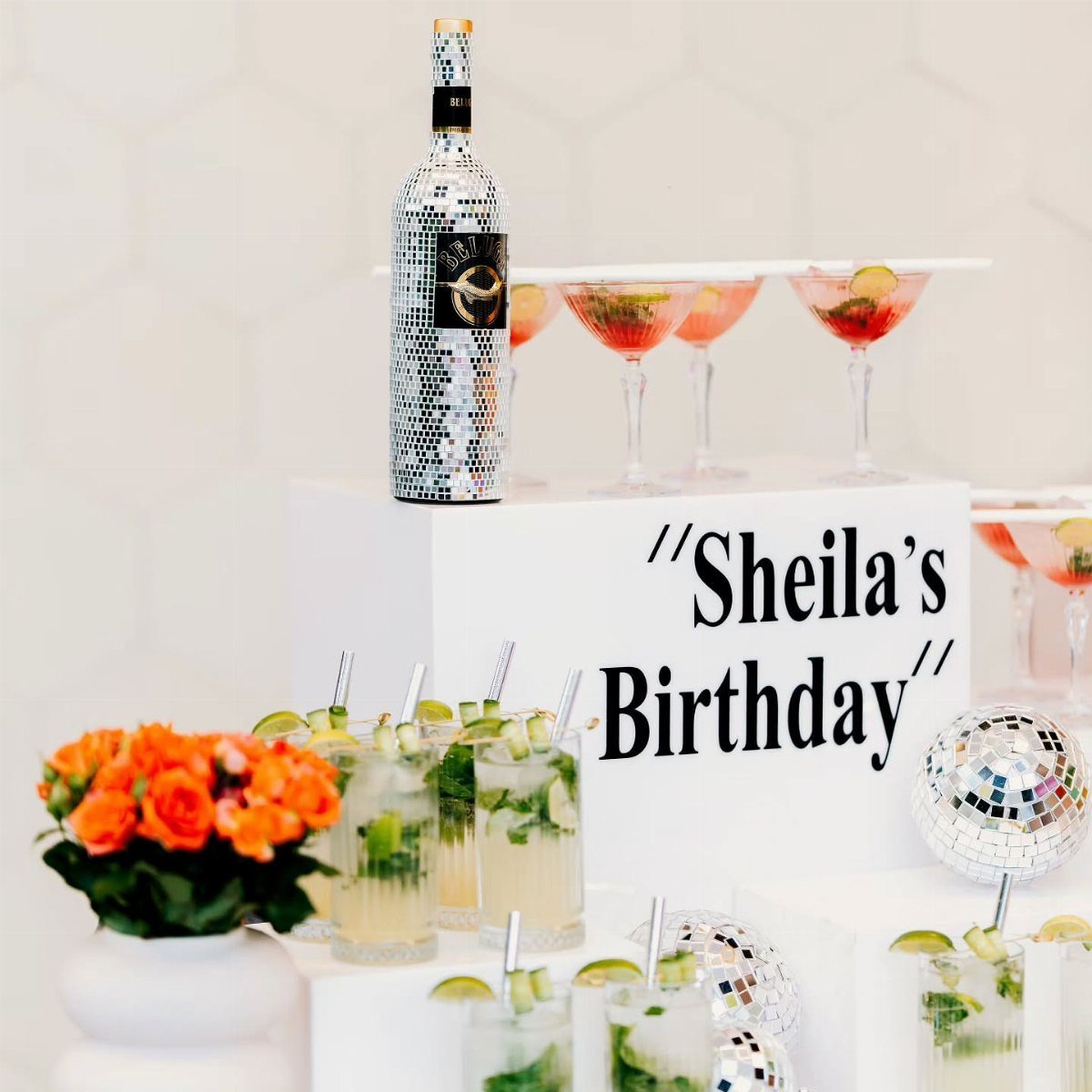 Birthday drink station with mojitos, red cocktails, and disco ball decorations on white tiers.